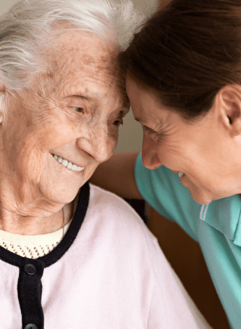 A young woman has her arm around an older woman, their heads are touching. 